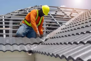 Roofer in a yellow hard hat and safety vest installing gray roof tiles during a full roof replacement after an insurance claim