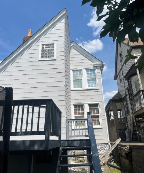 Gray residential house with energy-efficient replacement windows and a wooden deck, showcasing exterior improvements for Pittsburgh homeowners.