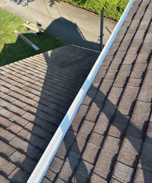 New white gutter with guard running along a shingle roof edge in Carnegie, Alan Construction