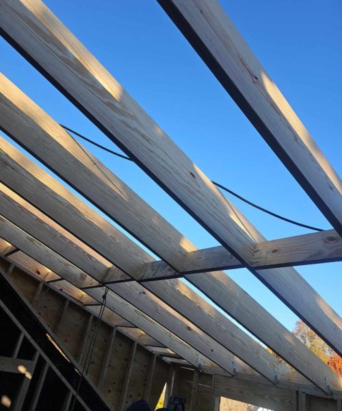 Wooden roof trusses under a clear blue sky, showcasing the framework for residential roofing installation by Alan Construction in Pittsburgh.